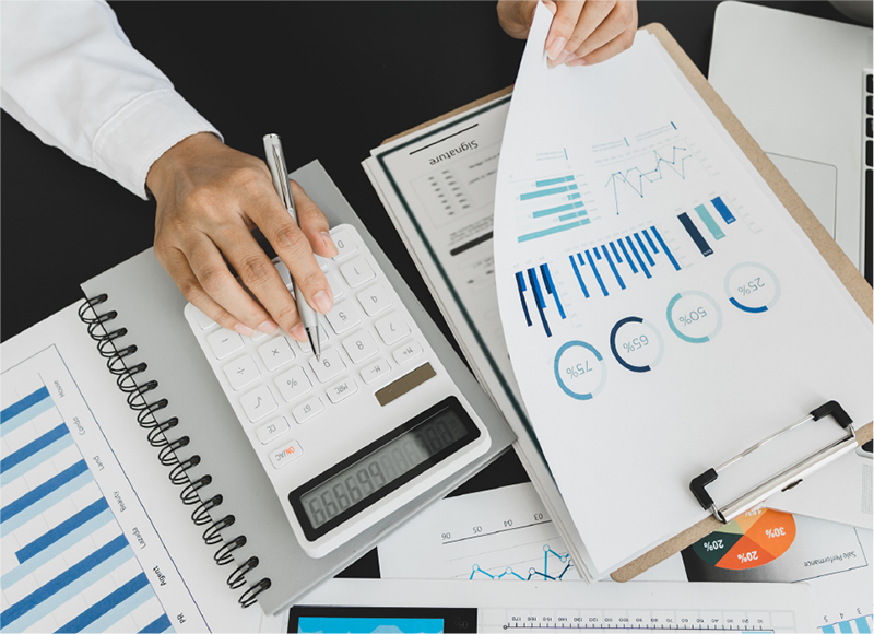The arms of a man sitting at a desktop filled with various graphs and a calculator