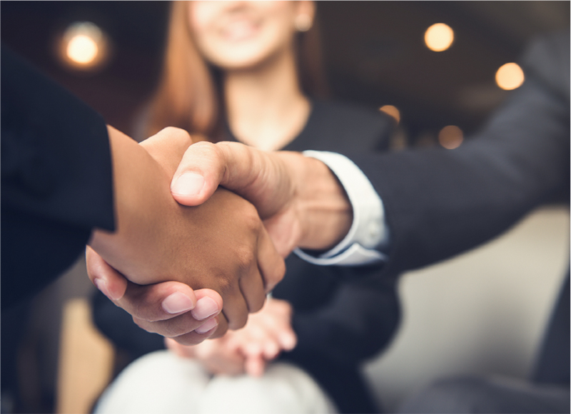 The arms of two business men wearing dark suits & shaking hands